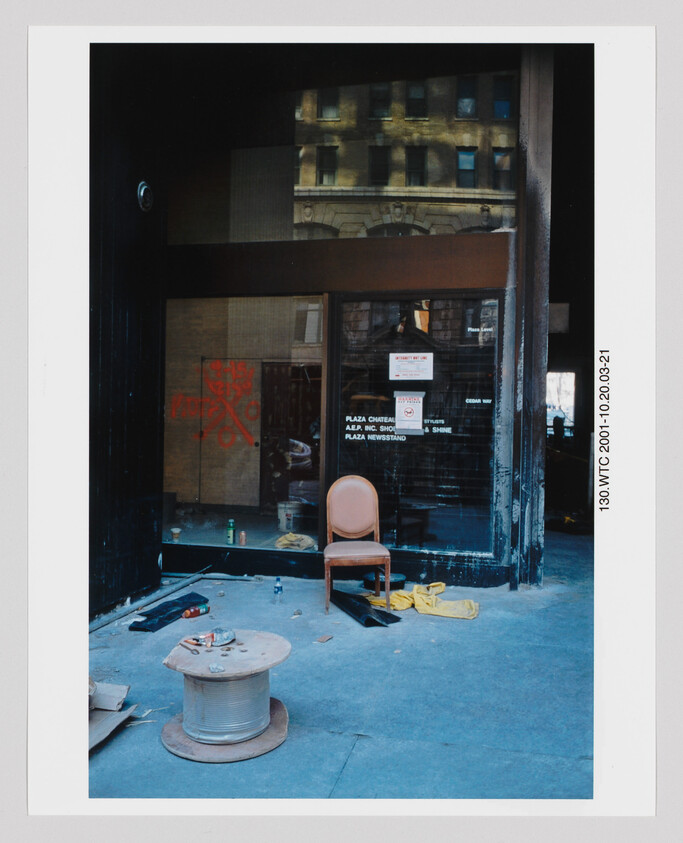 A single chair sits among construction debris outside a dark storefront window.