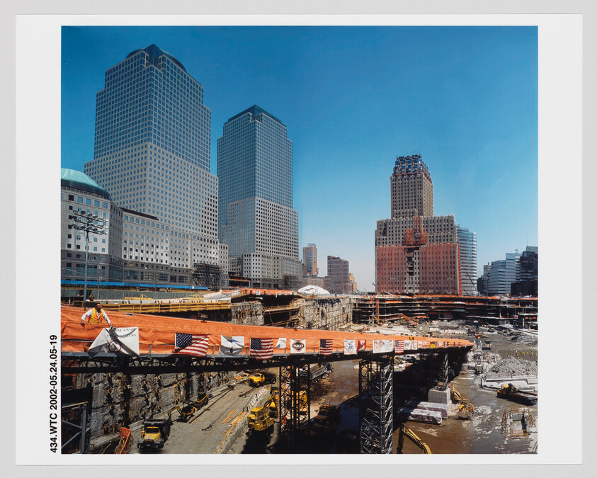 Large downtown construction site with cranes and workers building a deep foundation next to high-rise towers.