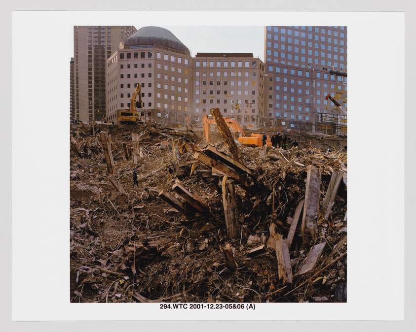 Heavy machinery and workers clear twisted steel and rubble at a large downtown disaster site.