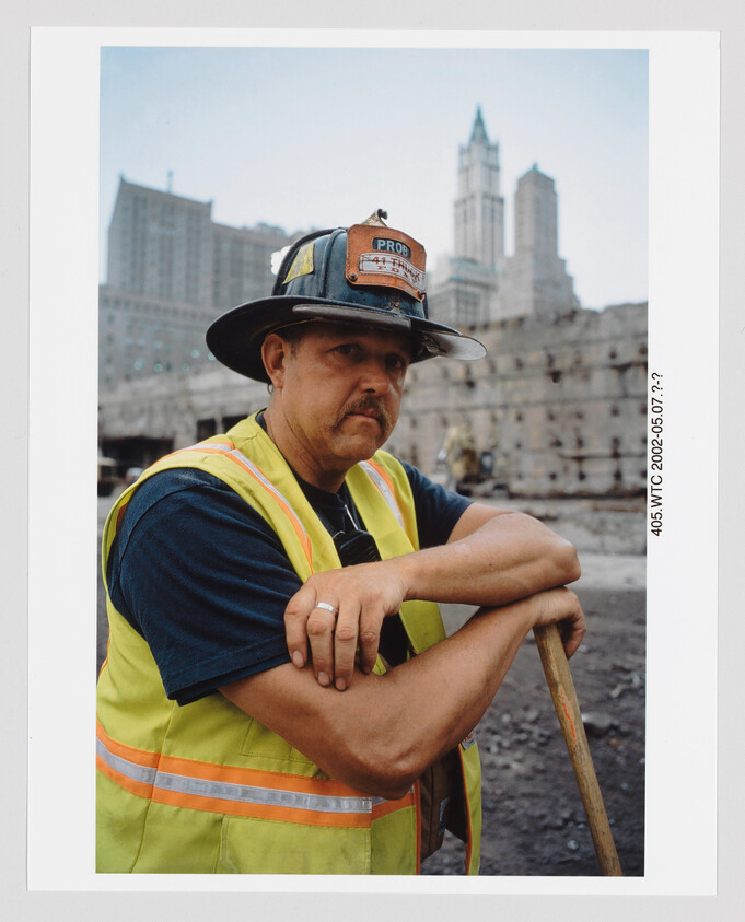 Construction worker in hard hat and safety vest leans on a shovel at a city worksite.
