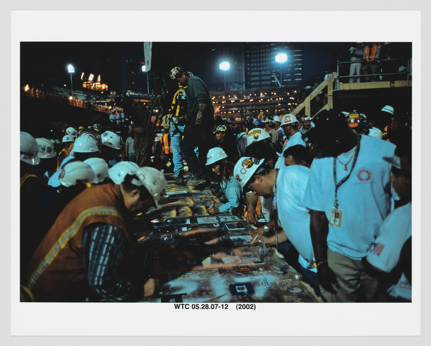 Construction and rescue workers wearing hard hats gather at a table inspecting and signing photographs at the WTC site.