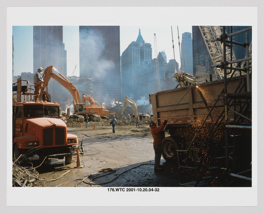 Workers and excavators clear debris while a worker uses a torch, sending sparks into the air.