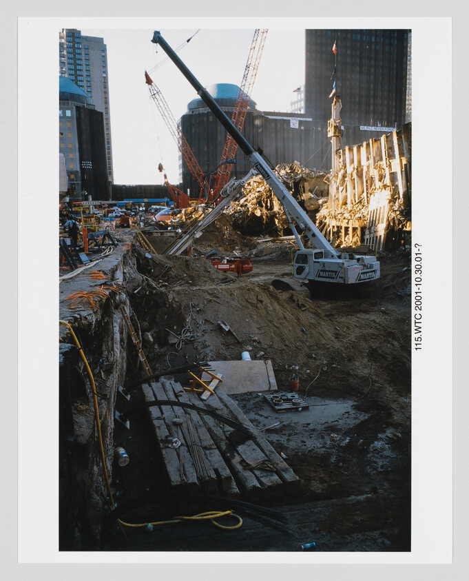 Large cranes and a crane-mounted excavator working in a deep urban construction and demolition site.