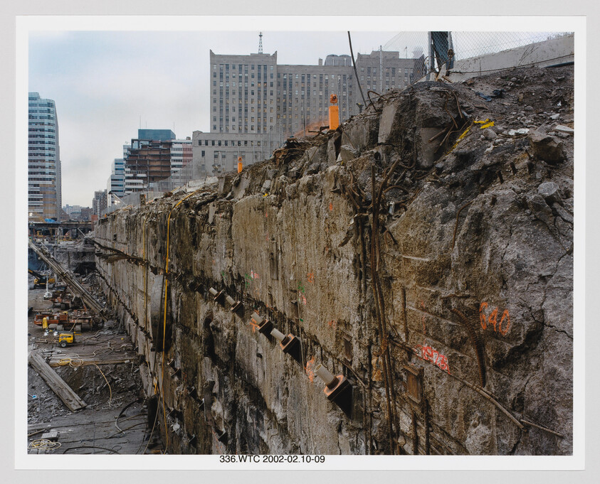Massive excavated concrete wall with exposed rebar and construction equipment at a downtown building site.