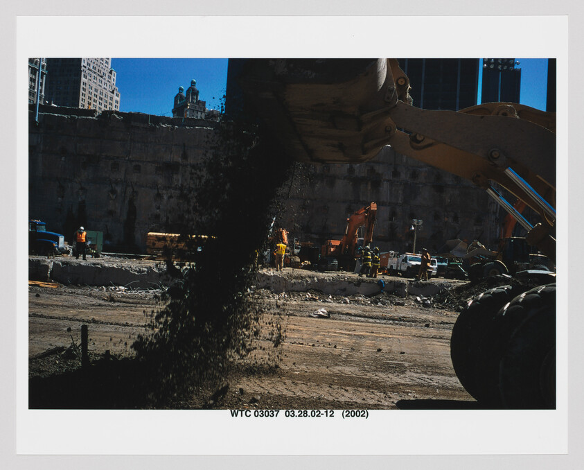 A construction excavator dumps dirt onto a busy worksite while crews operate heavy equipment.