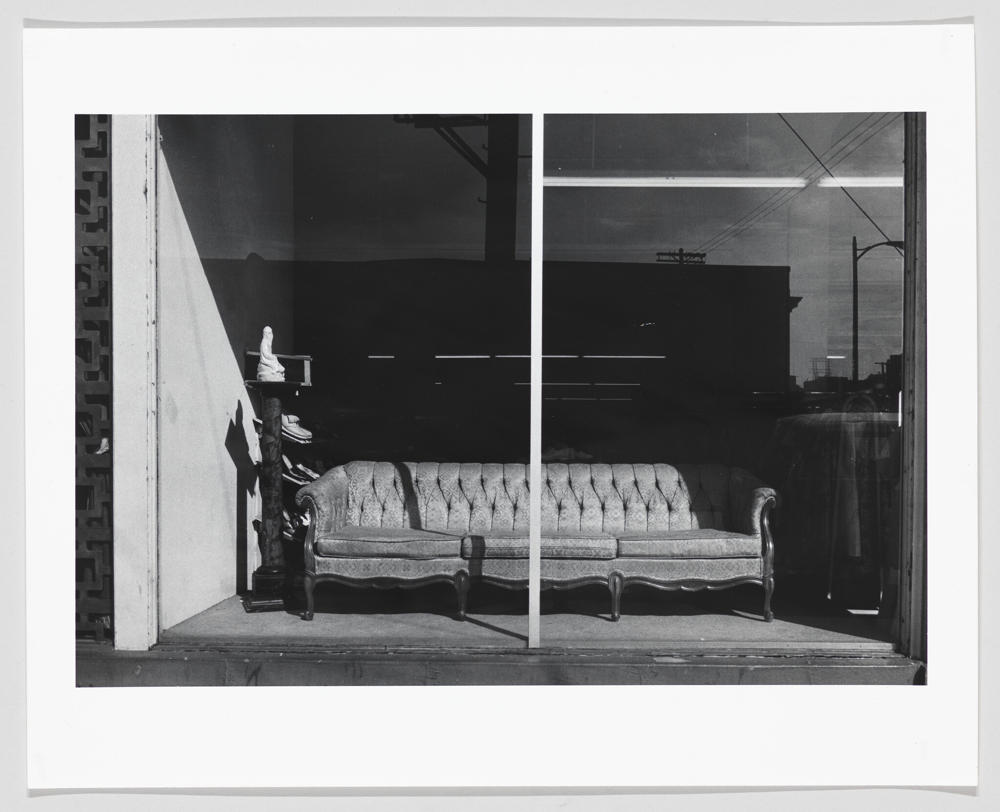 A vintage tufted sofa sits on display behind a large store window with reflections.