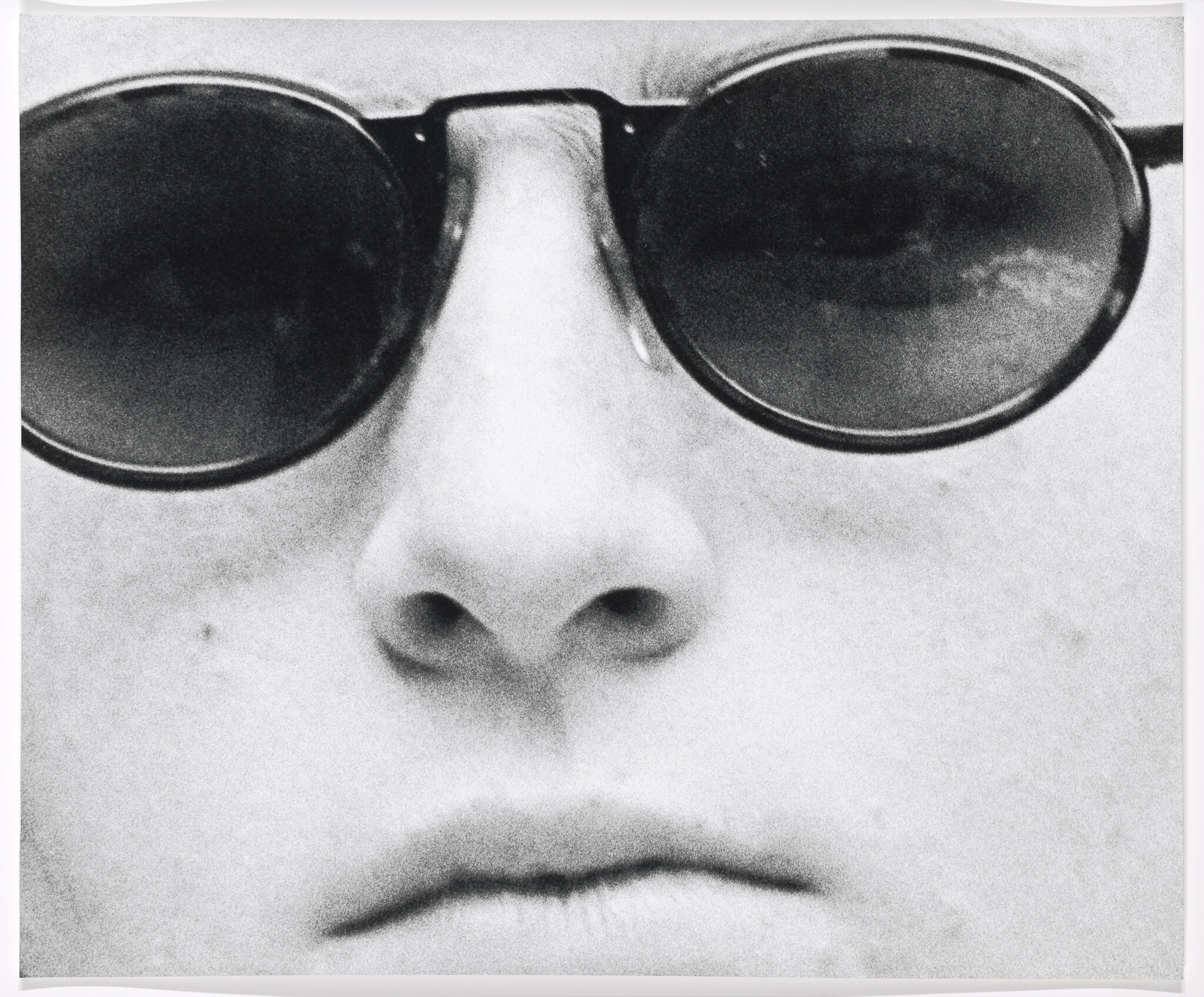 A person's face wearing round sunglasses, focusing on the nose and closed lips.