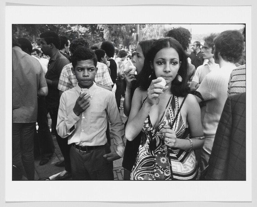 Young woman and boy eat ice cream while standing in a crowded outdoor gathering.