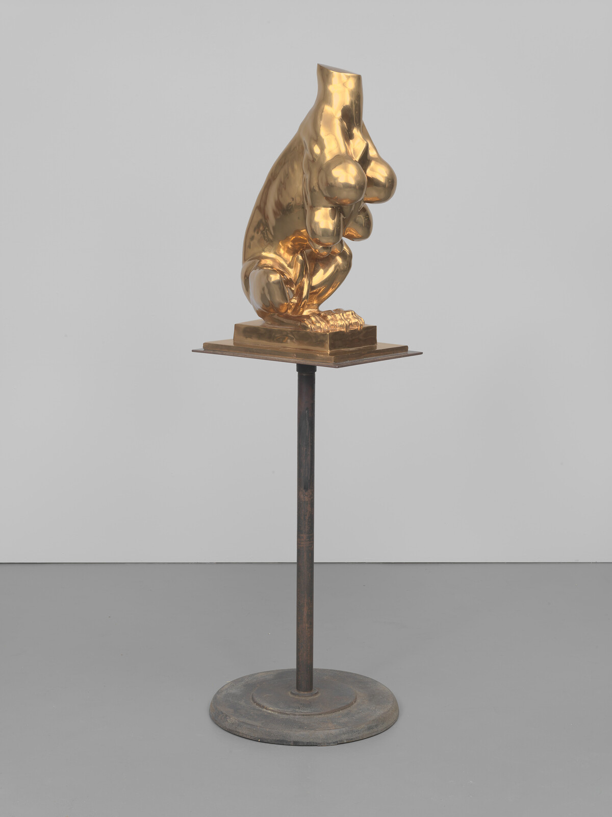 A polished golden sculptural torso with breasts and crouching legs displayed on a metal pedestal.
