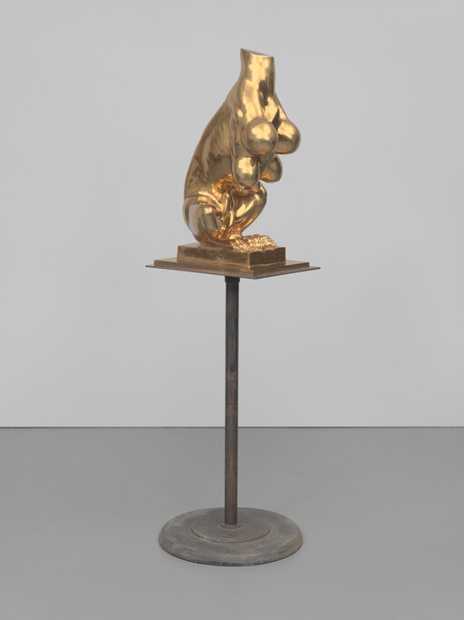 A polished golden sculptural torso with breasts and crouching legs displayed on a metal pedestal.