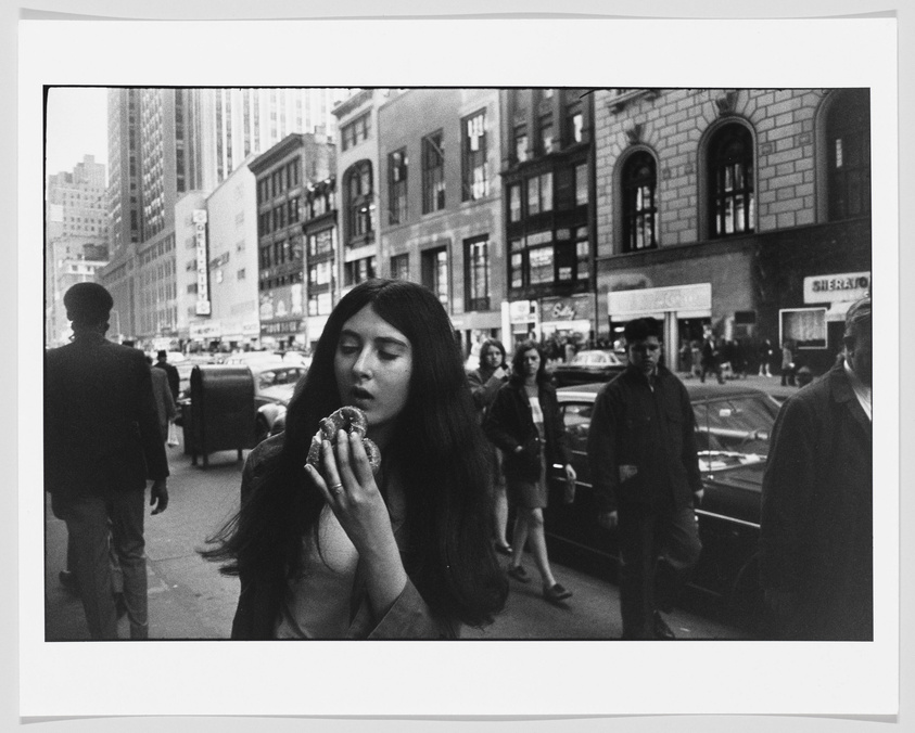 In the middle of a busy street, a young woman looks down at a soft pretzel.