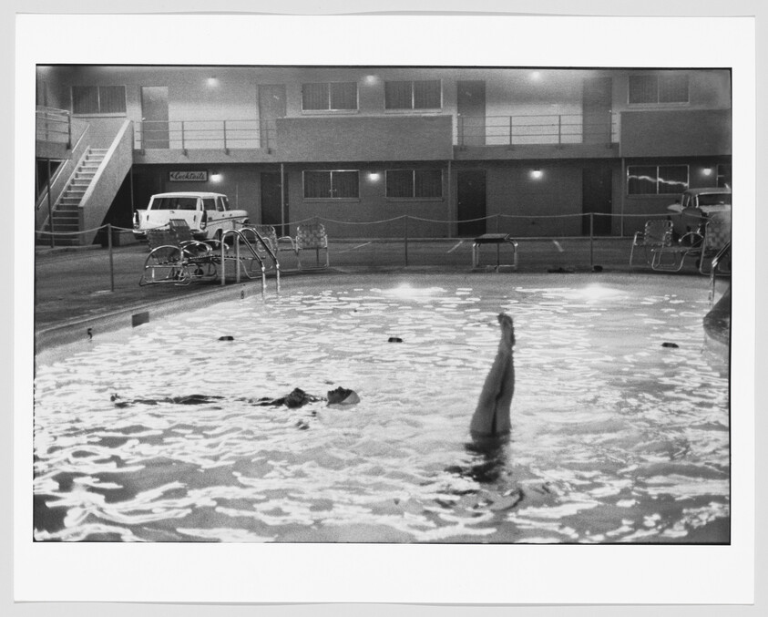 Two women in a motel pool at night, one floating face-up and one with legs raised vertically.