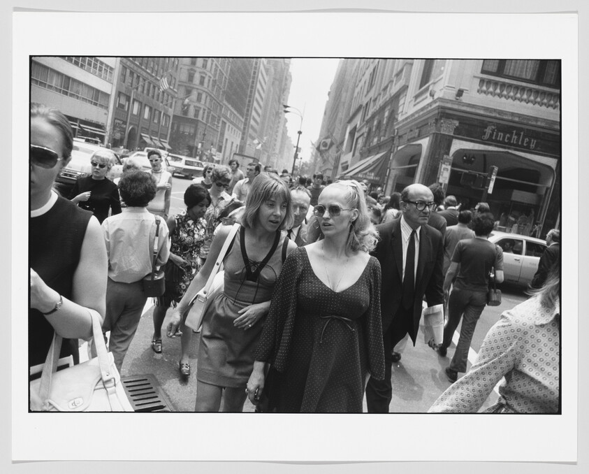 Two women walk through a busy city sidewalk among a crowd of pedestrians.