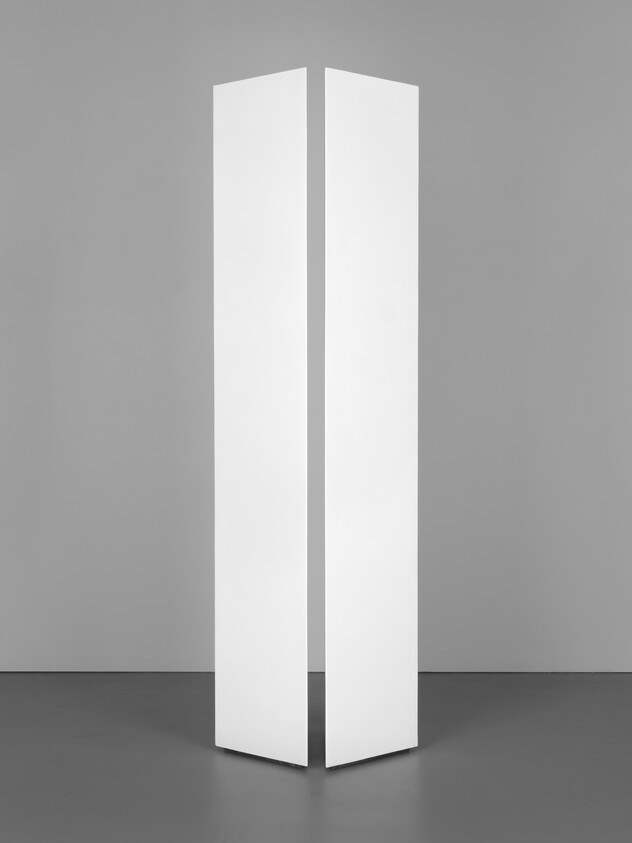 A minimalist white vertical sculpture with a sharp fold in the center, set against a gray background.