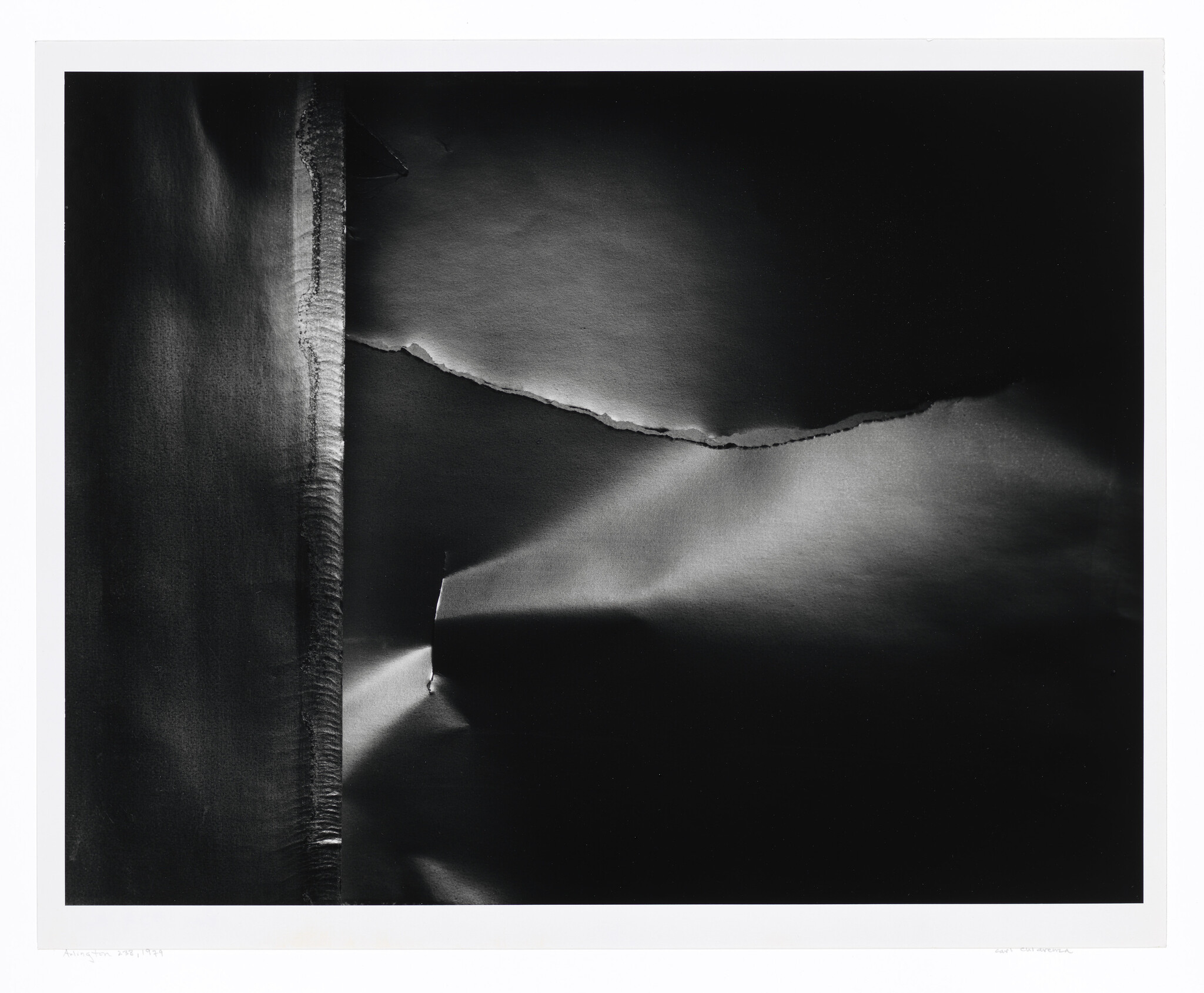 A torn sheet of dark paper with a vertical seam and a jagged horizontal tear lit by soft light.