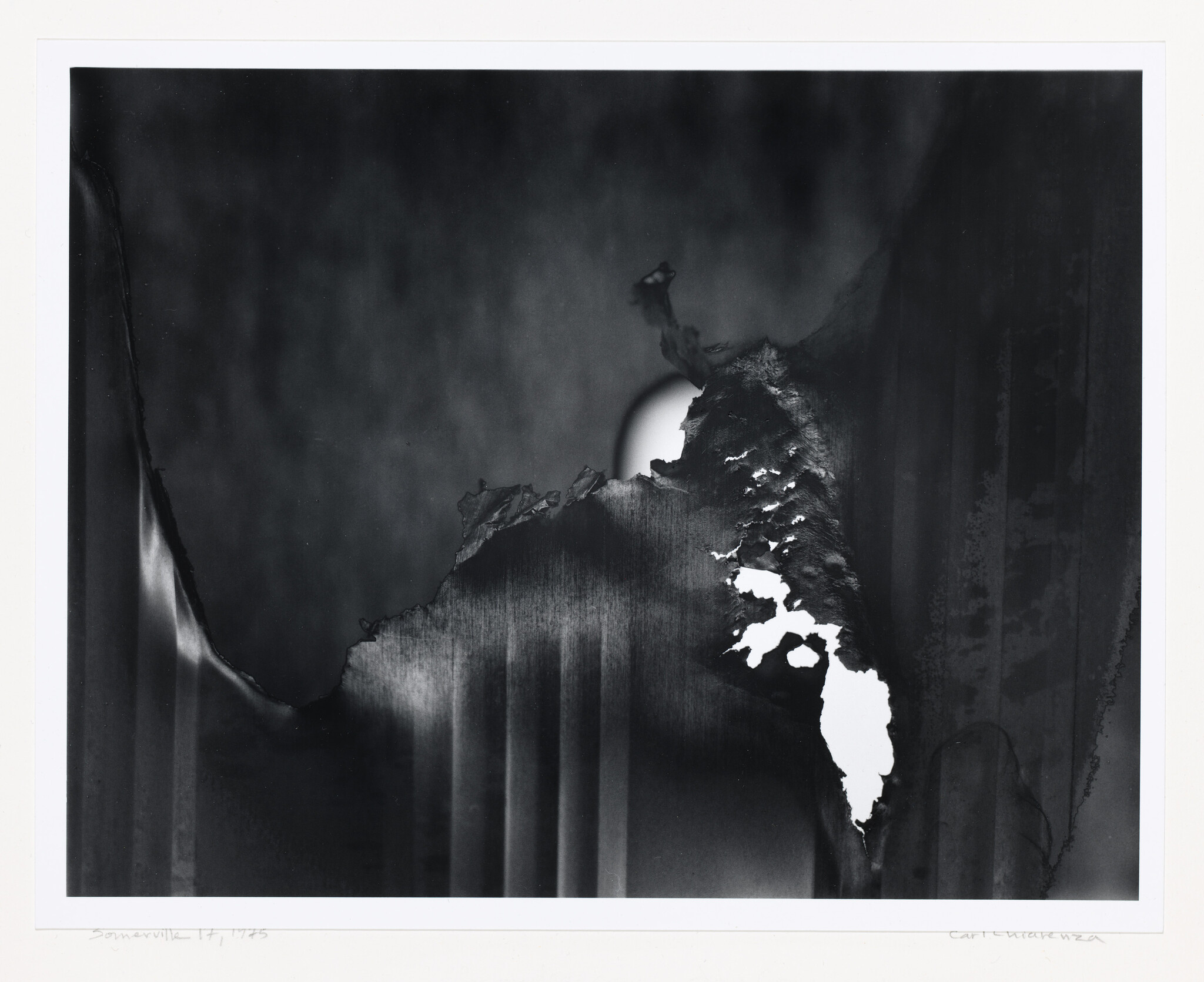 Torn, charred paper reveals a bright circle of light behind a dark textured surface.