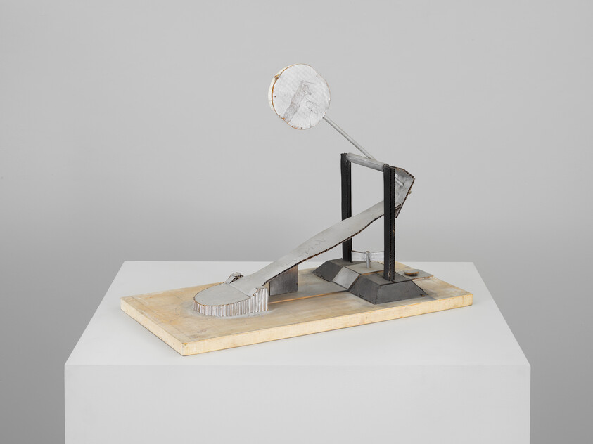 Small abstract metal sculpture with a tilted ramp and circular disk on a wooden base.