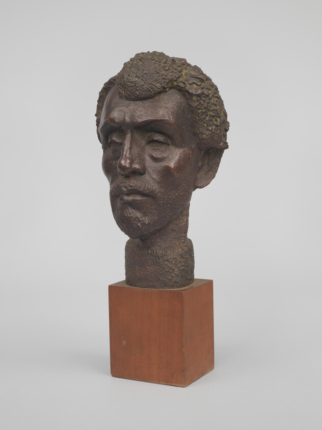 Bronze sculpture of a man's head with textured hair mounted on a wooden block.