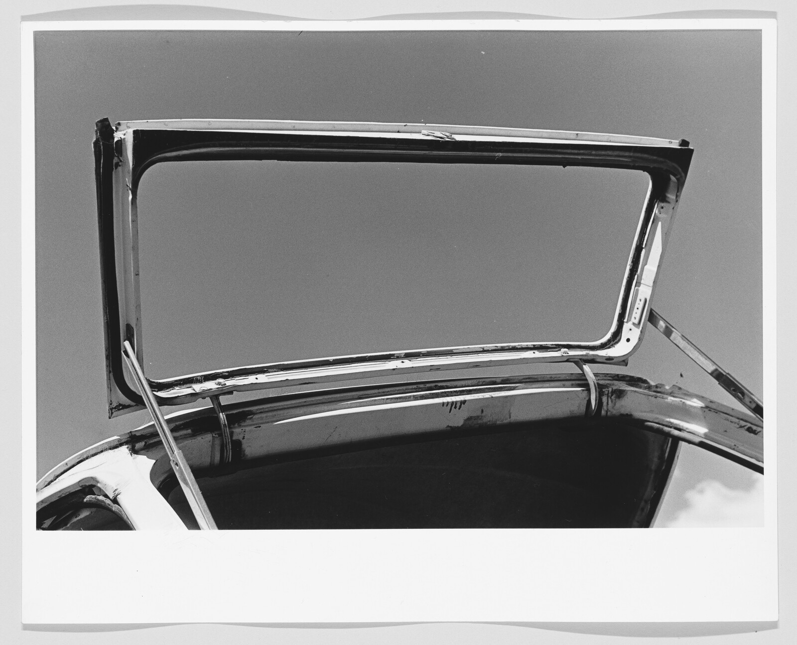 Car trunk lid propped open against clear sky, showing metal hinges and frame.