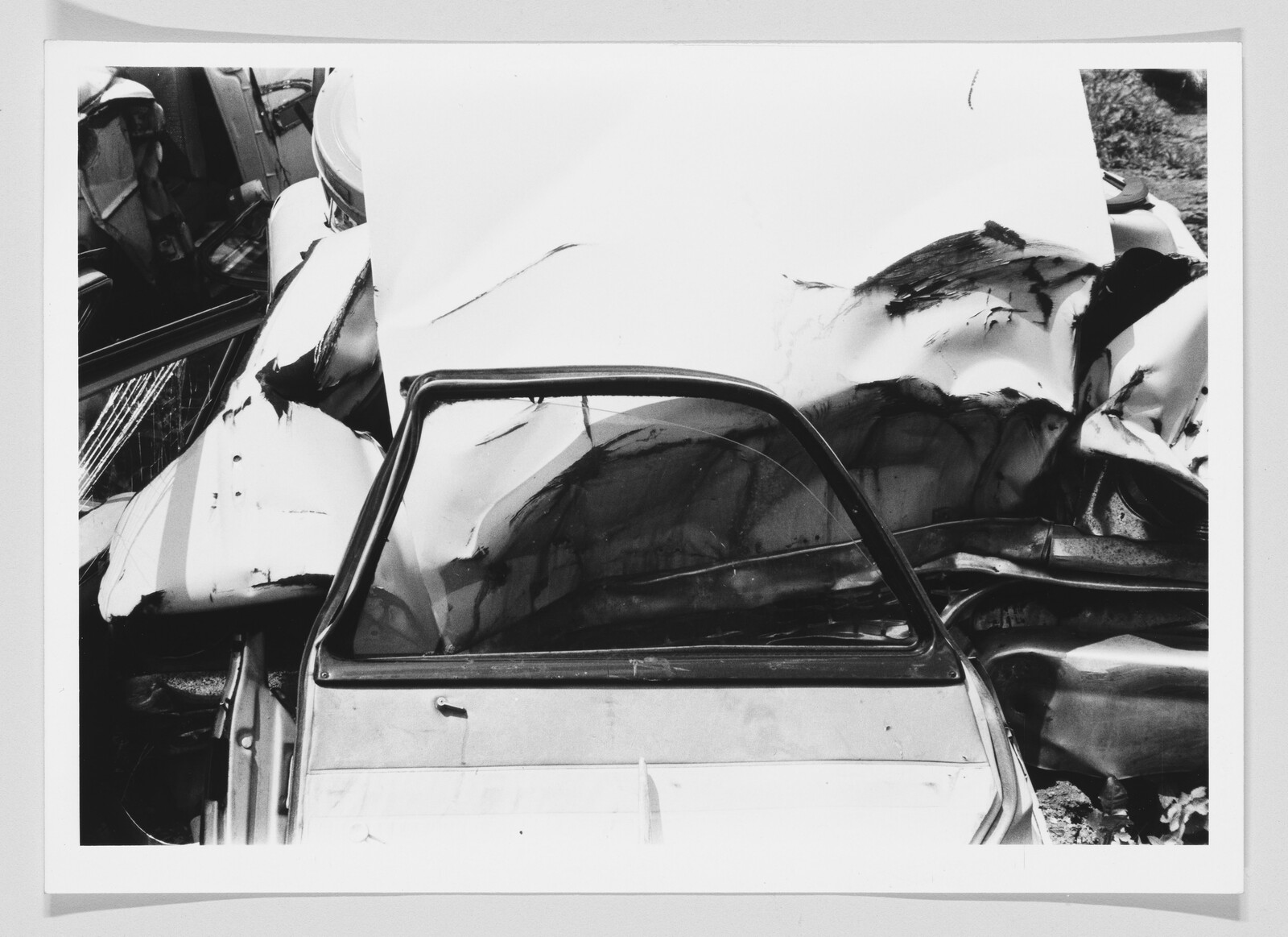 A crushed car door and shattered window pushed against a heavily damaged white car hood.