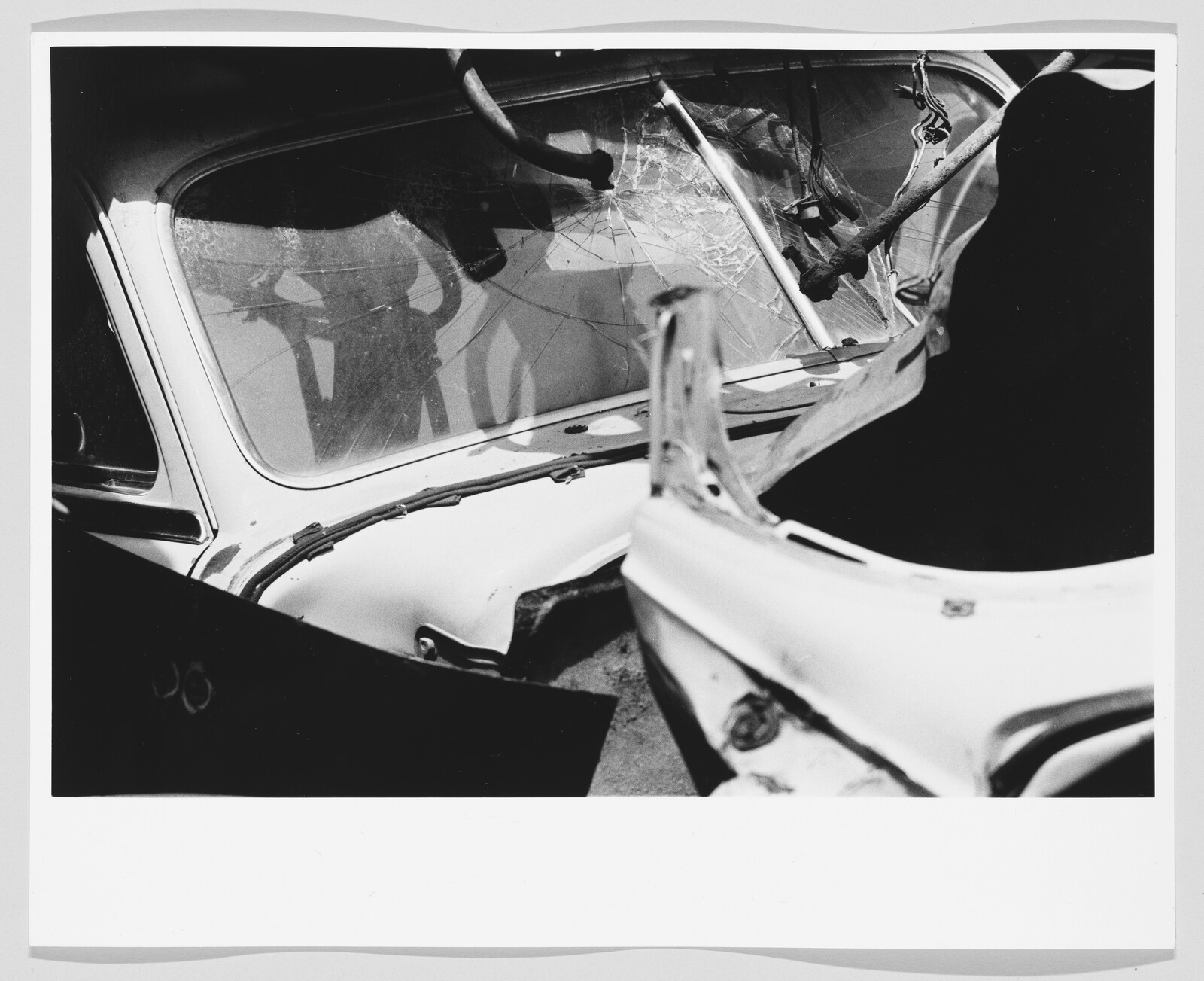 Damaged car interior with shattered windshield and a broken steering column twisted by a lodged tree branch.