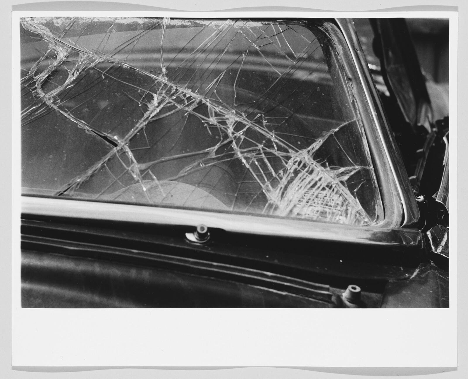 A car windshield with extensive spiderweb cracks and a dented frame from a collision.