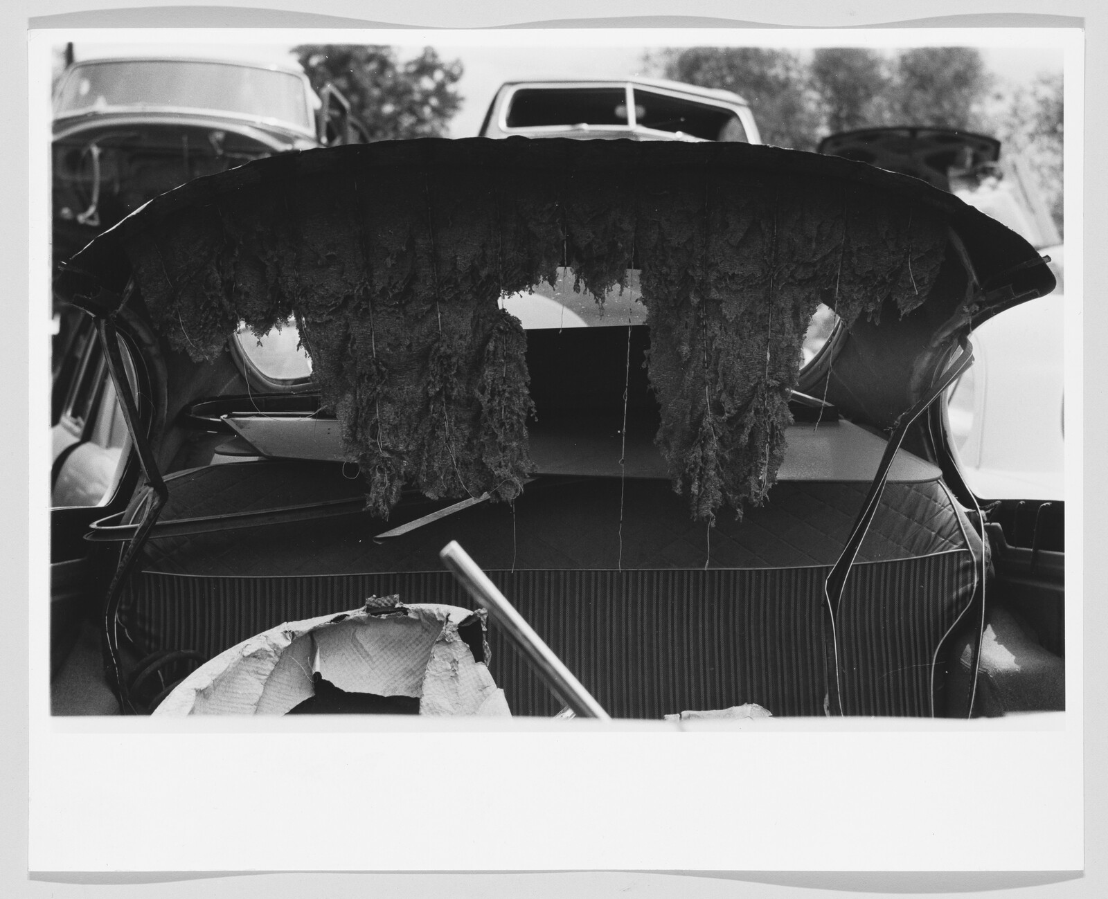 Torn car trunk lining hangs down over the open trunk filled with discarded parts.