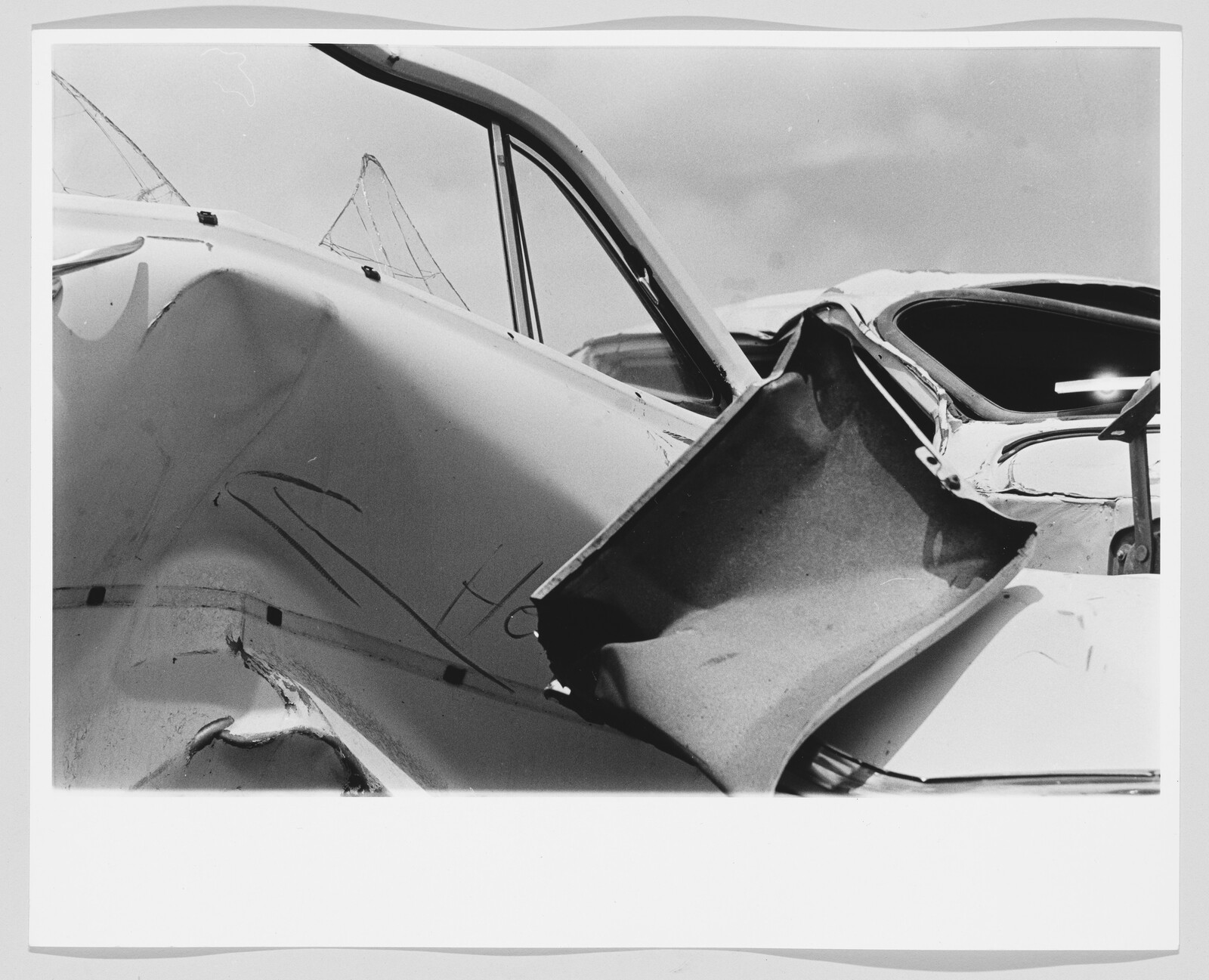 Crumpled white car door and shattered windshield from a severe collision.