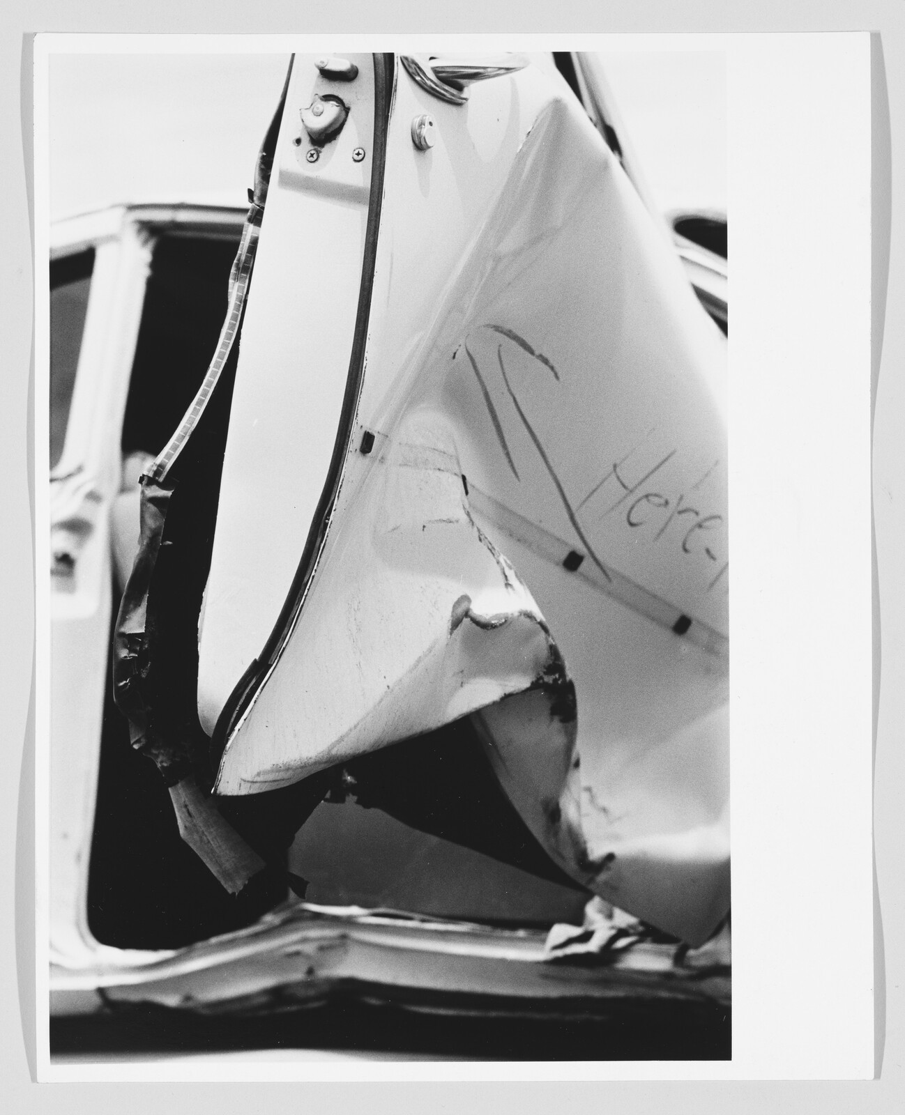 Crushed white car door with deep dents and handwritten note saying "Here".