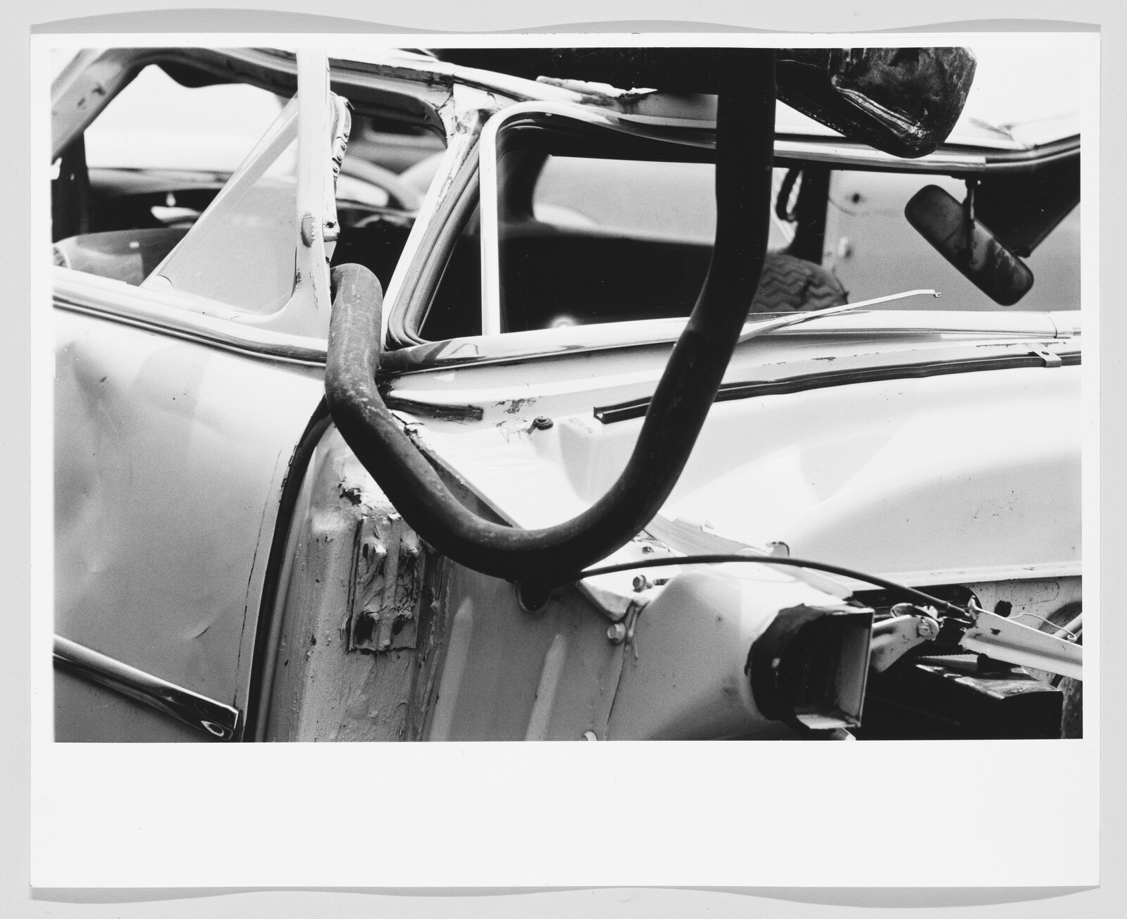 Crumpled car door and windshield with a large rubber hose draped across the wreck.