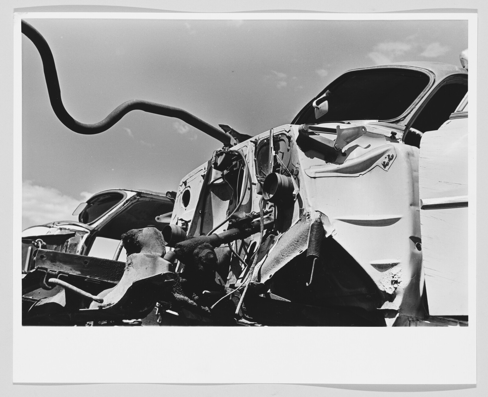Crumpled car front with exposed engine parts and a bent exhaust pipe under the sky.