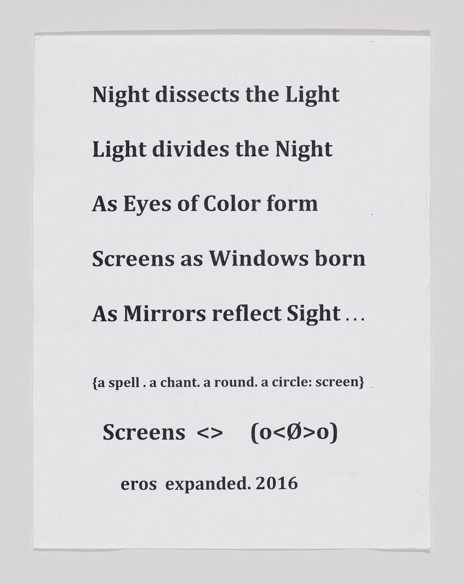 A printed sheet of paper with a poem or text that reads: "Night dissects the Light / Light divides the Night / As Eyes of Color form / Screens as Windows born / As Mirrors reflect Sight... / {a spell . a chant . a round . a circle: screen} / Screens <=> (o<Ø>o) / eros expanded. 2016". The text is in a simple, sans-serif font, centered on the page.