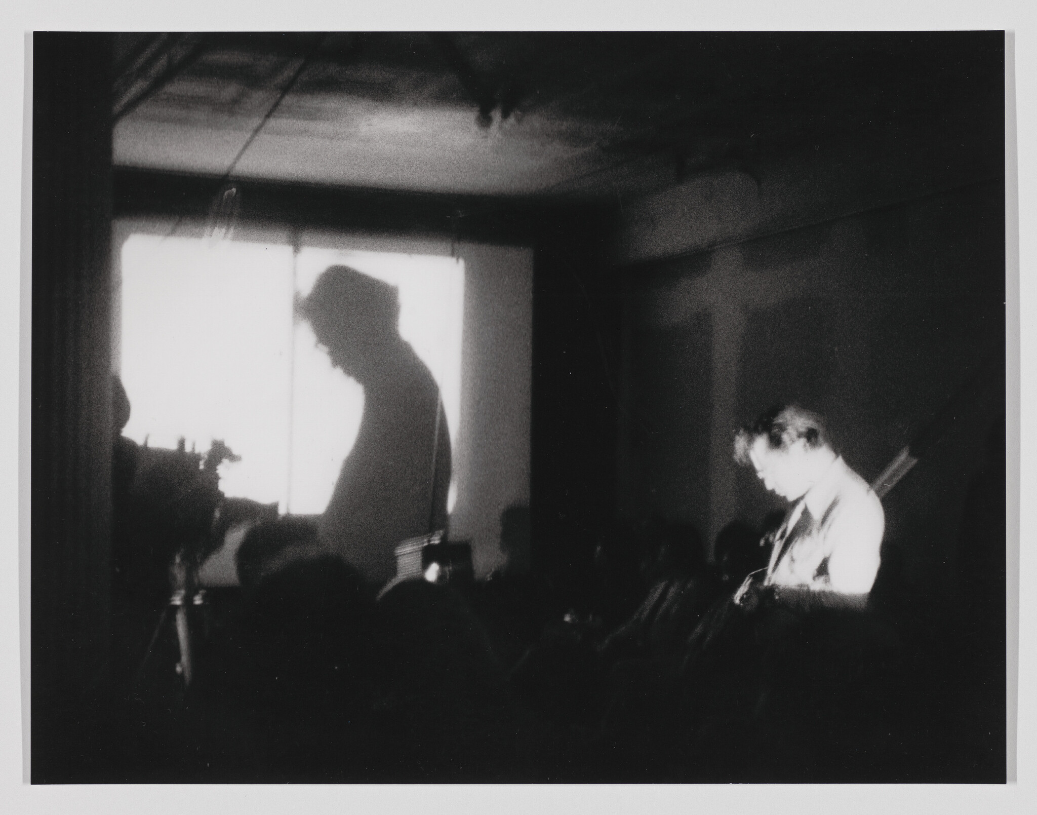 Person playing guitar in a dimly lit room, with their shadow projected on a screen.