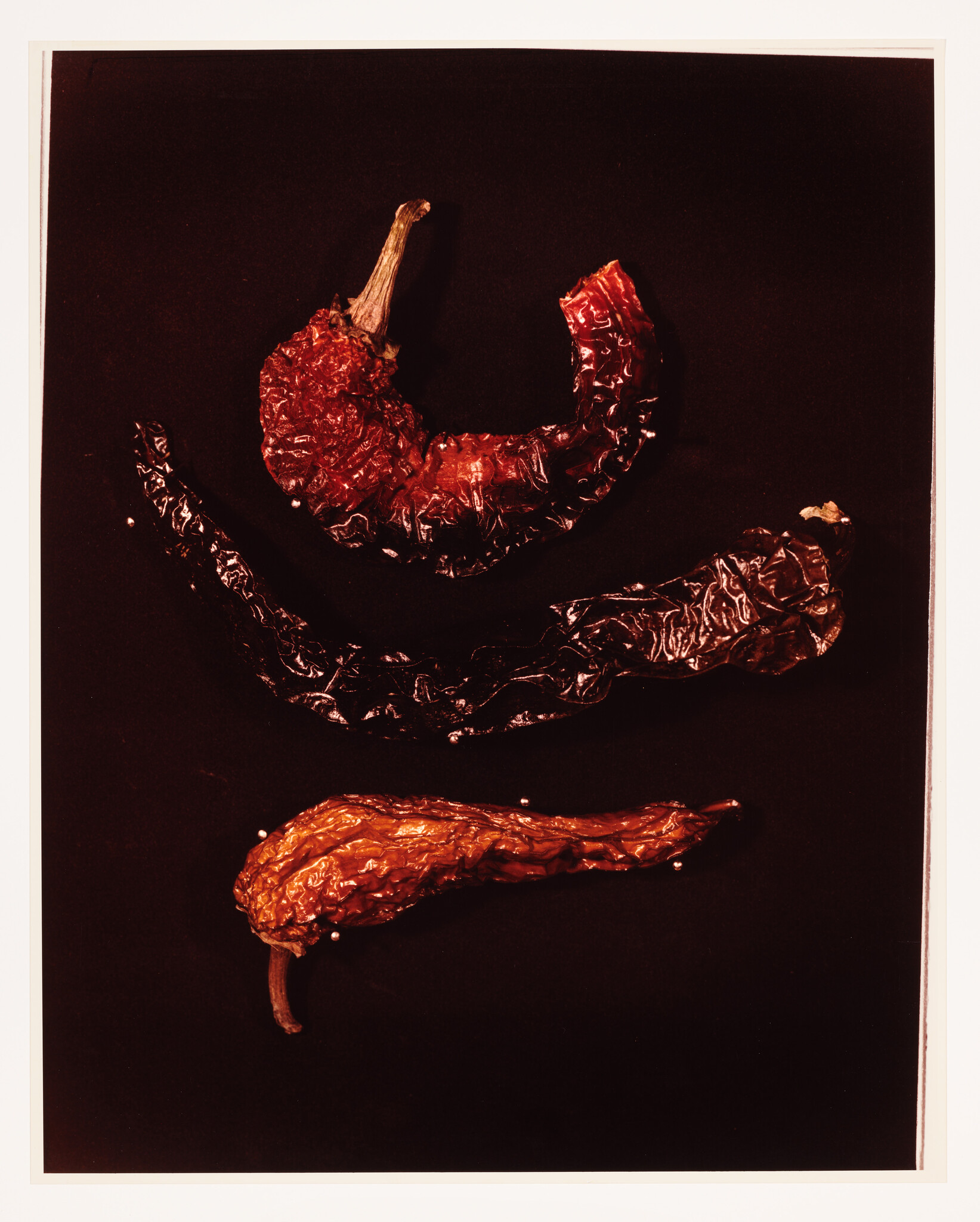 Three dried red chili peppers arranged vertically on a dark background.