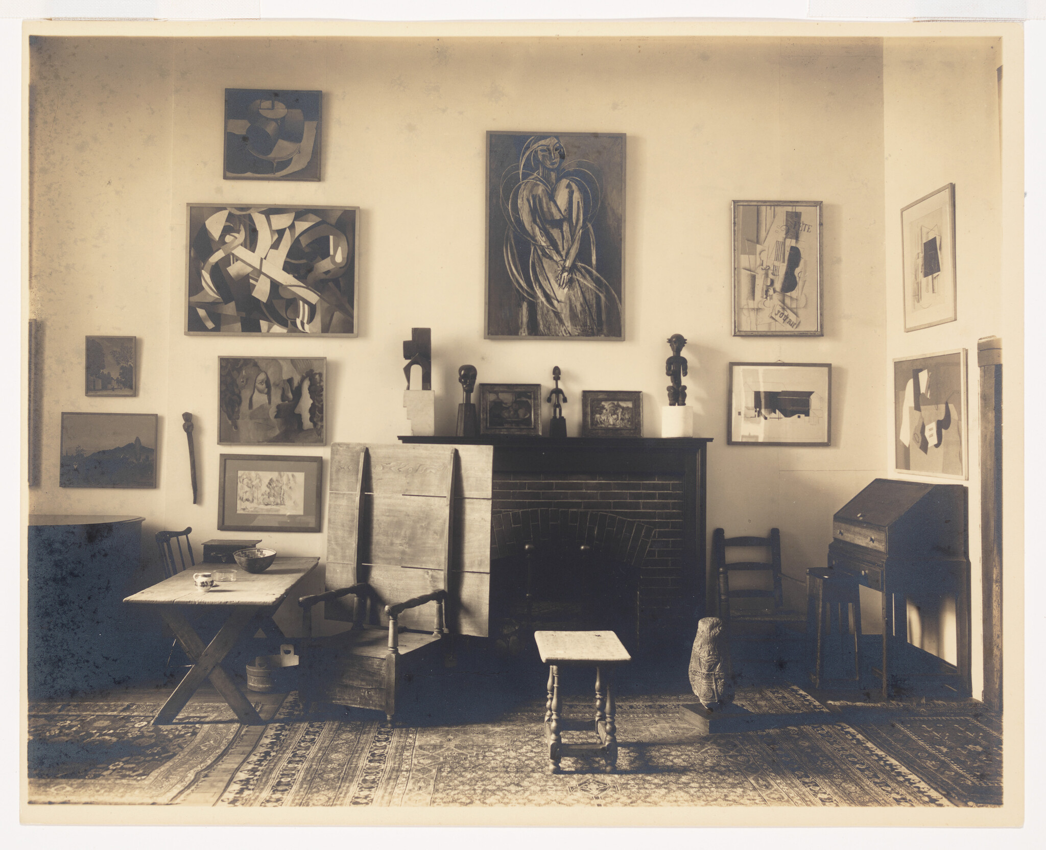 Living room with a fireplace and walls covered in framed abstract paintings and wooden furniture.