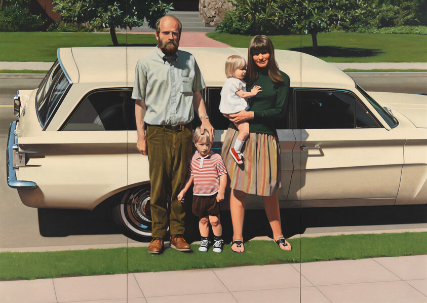 A family of four stands in front of a vintage car on a sunny day.