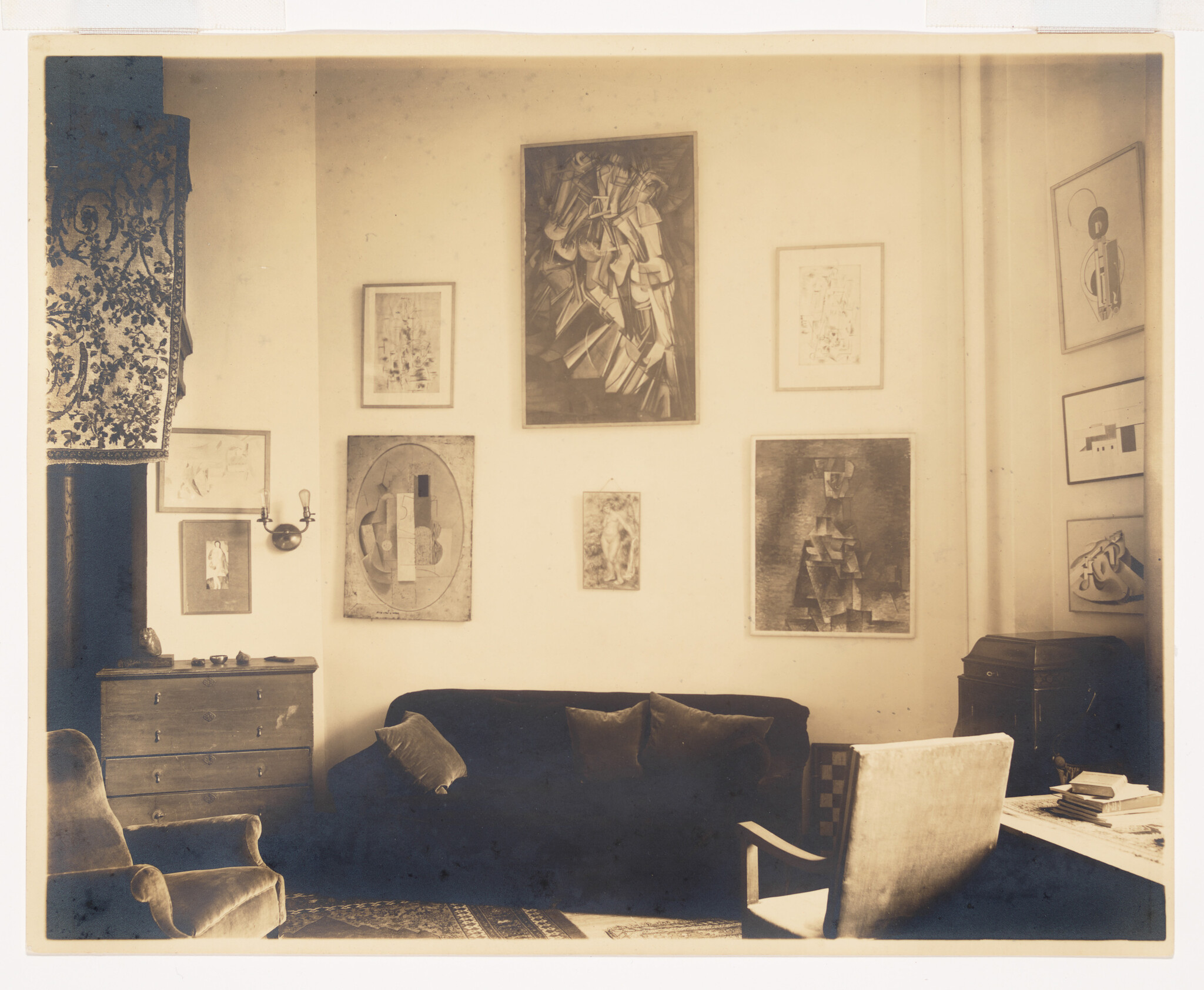 A cozy living room with a sofa, armchairs, and several framed abstract artworks on the wall.