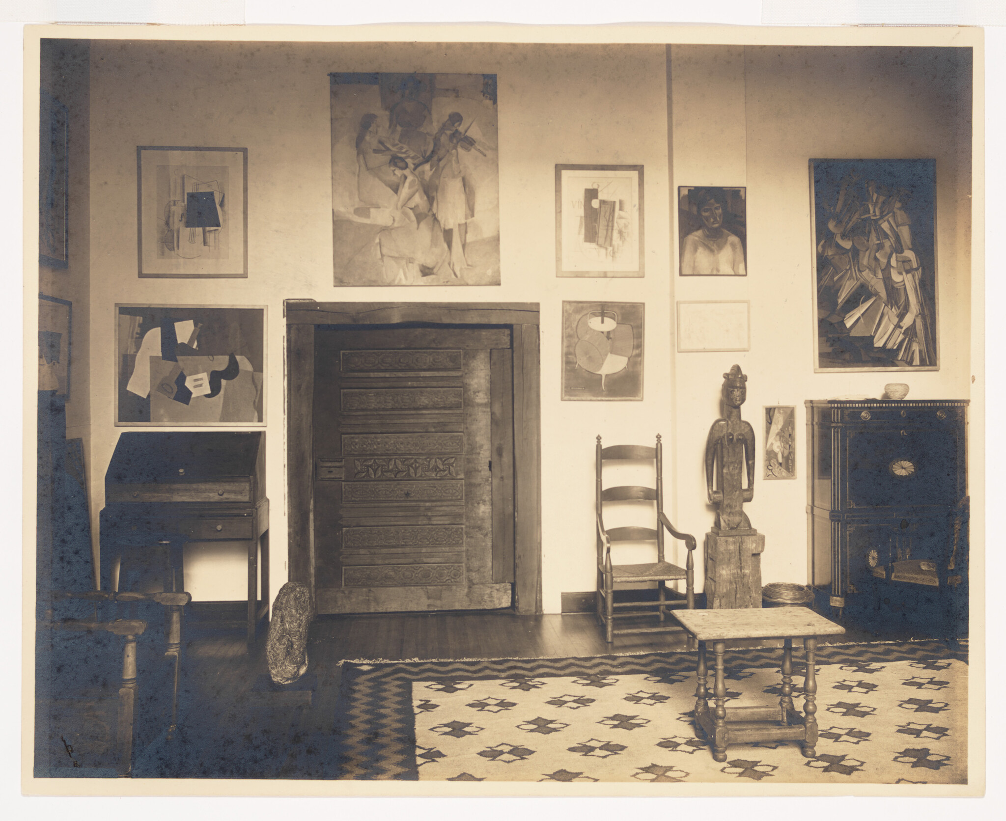 A room with a carved wooden door flanked by chairs, artwork, a small table, and a statue.