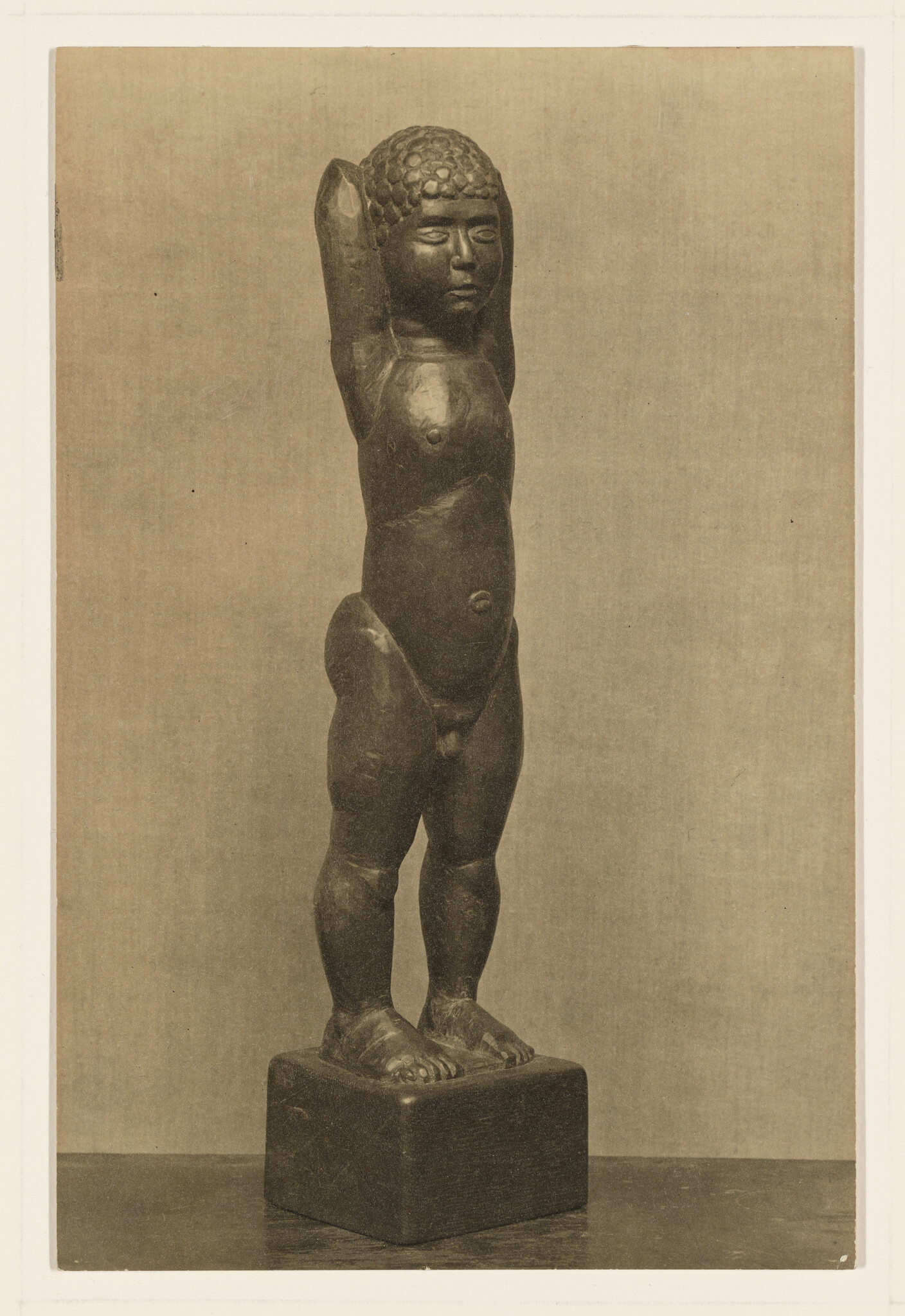 A small carved standing nude child statue with raised arms mounted on a square base.