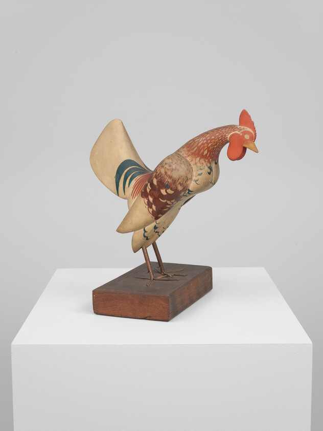 A wooden rooster leaning forward on a small platform and fading in color