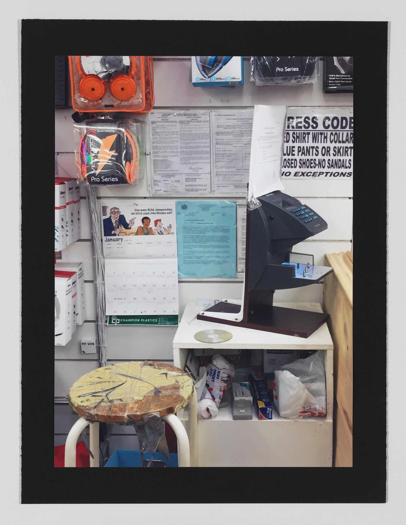 Worn wooden stool sits in front of a wall-mounted time clock and cluttered back-counter supplies.