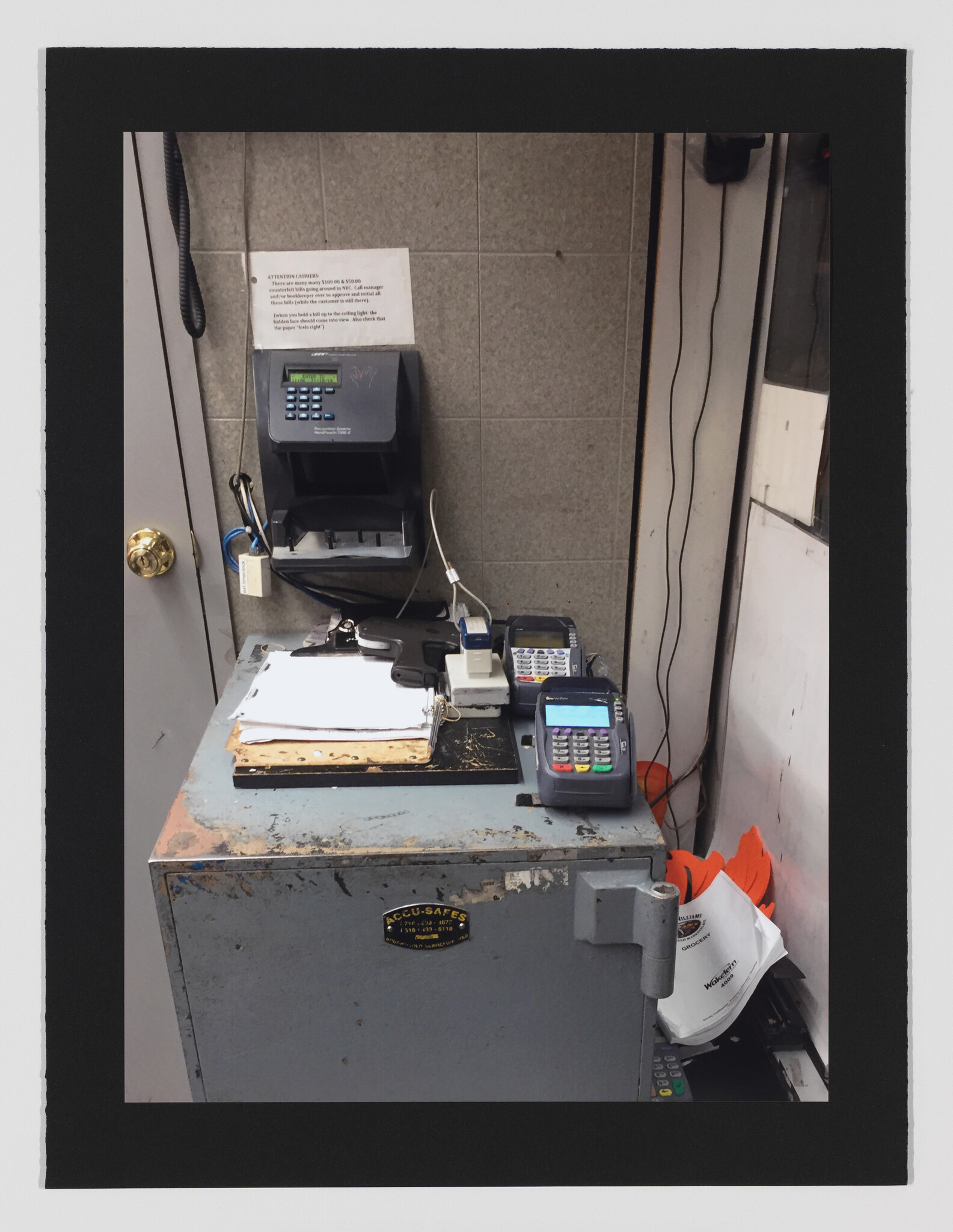 Worn metal safe used as a cashier workstation with card terminals, clipboard, and time clock on the wall.