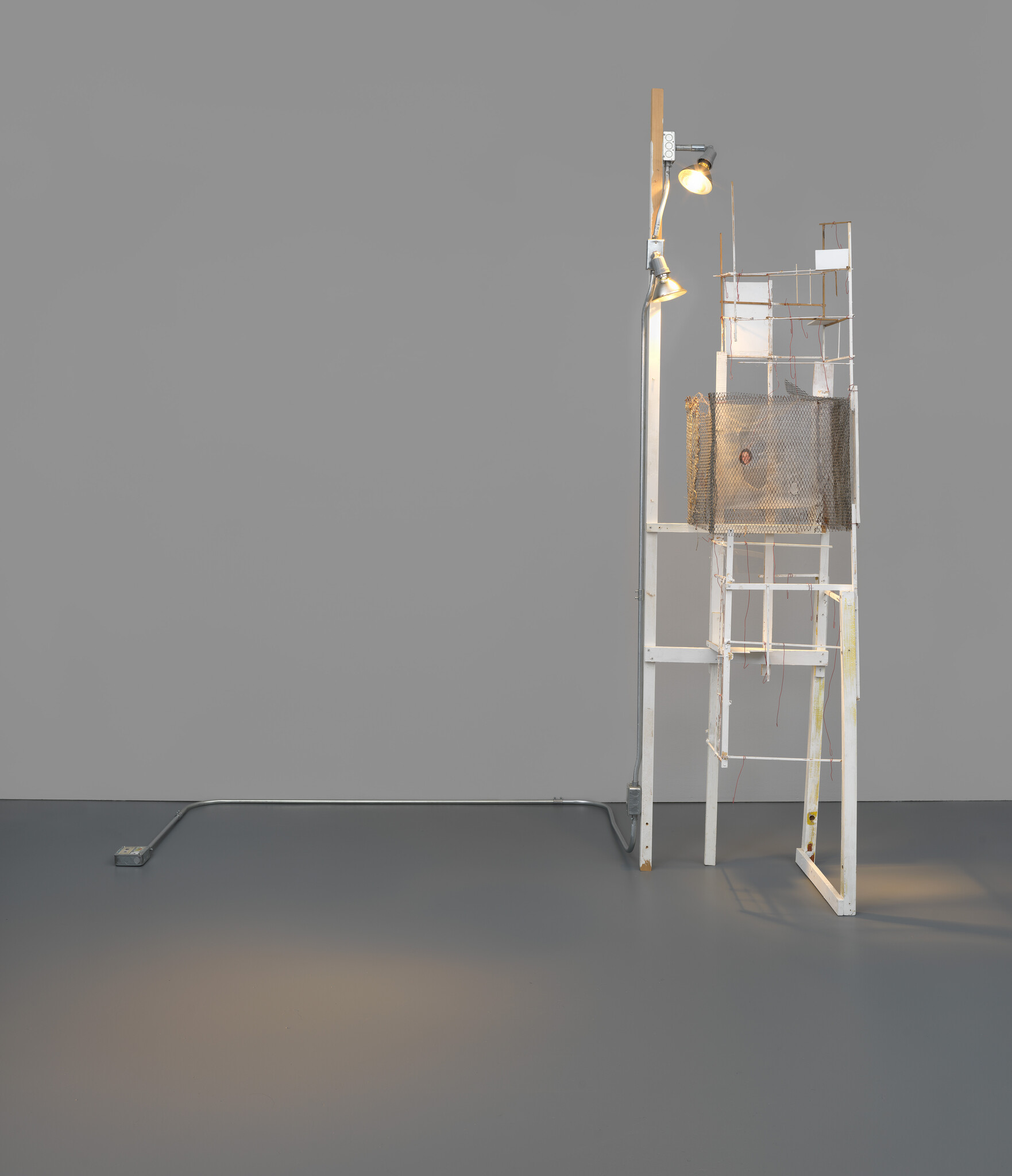 A tall white wooden frame with mesh and spotlights casts a warm pool of light on the floor.