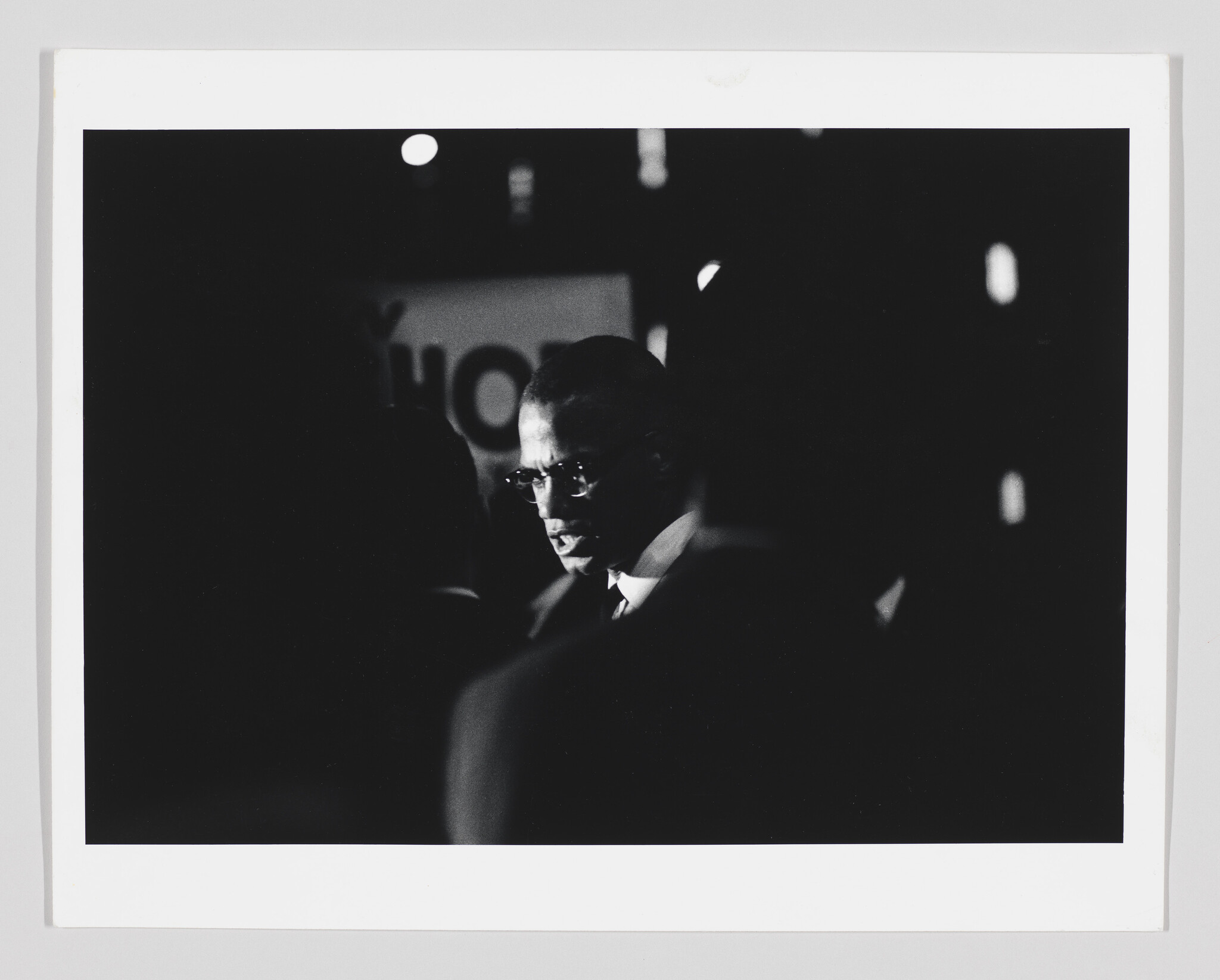 A man wearing glasses speaks intensely to people in a dark, crowded space.