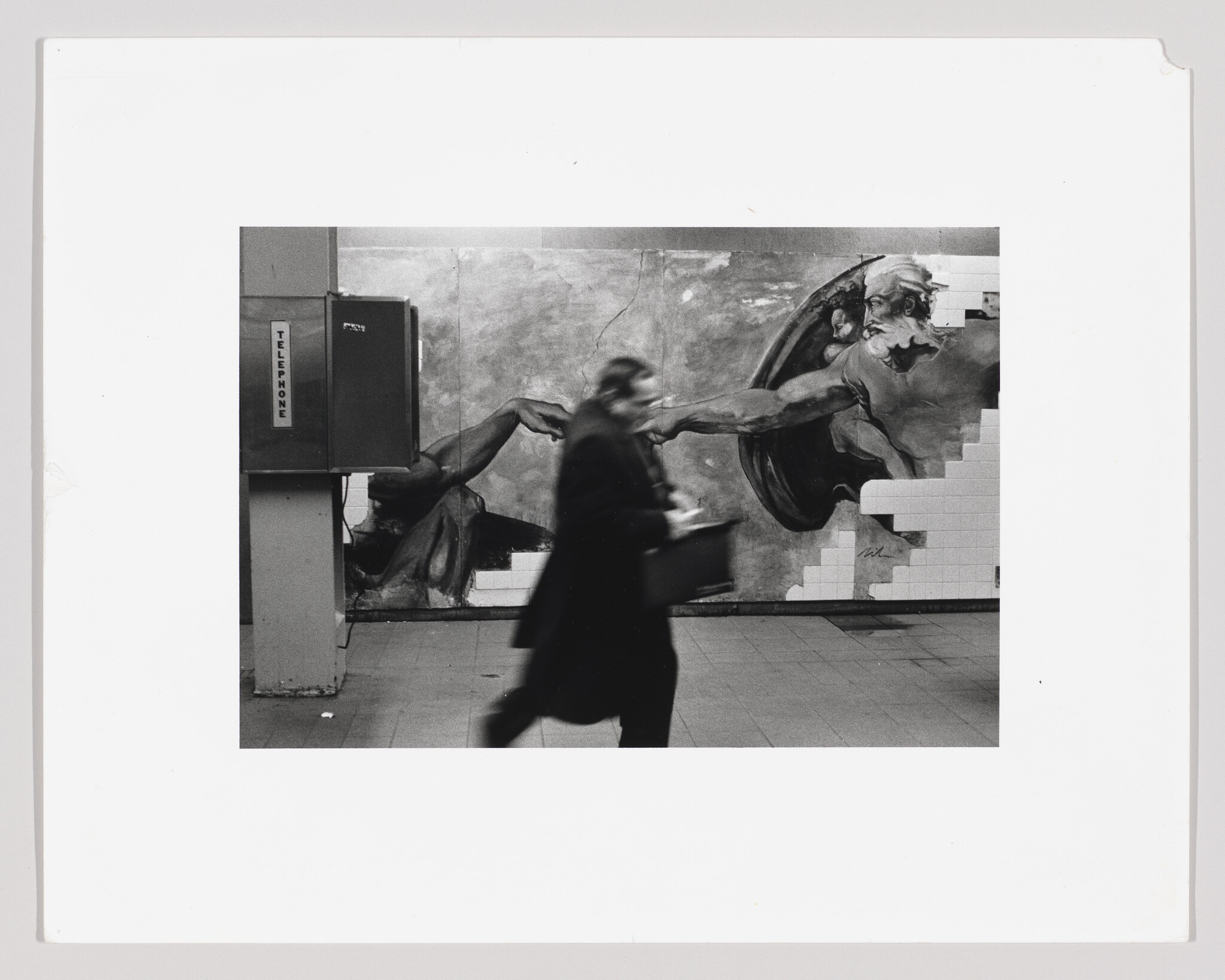 Blurred man hurries past a mural of outstretched hands while walking by a subway payphone.