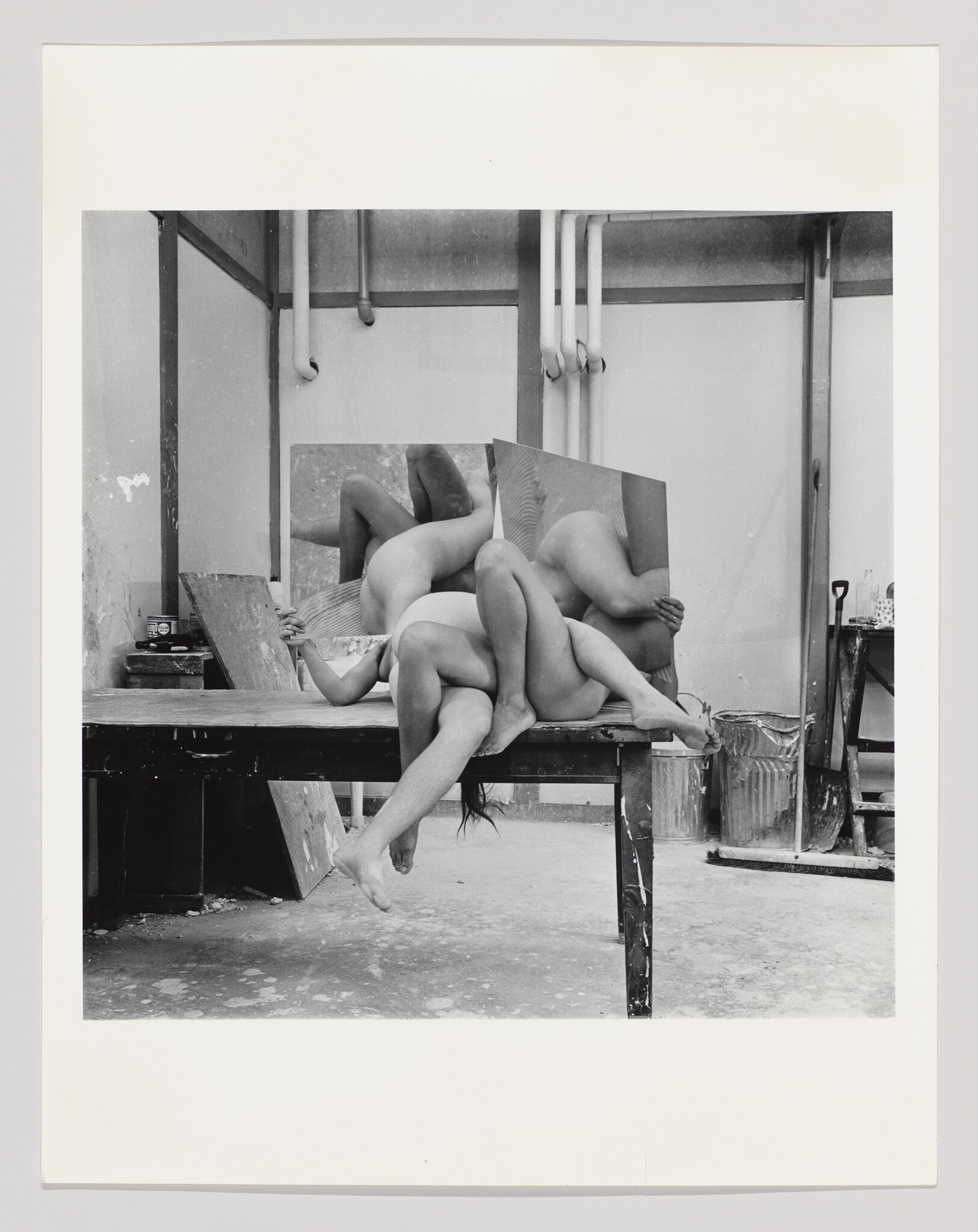 Several nude bodies are intertwined on a studio table with mirrors reflecting their forms.