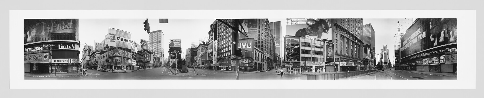 Wide empty Times Square street surrounded by tall buildings and large advertising billboards.