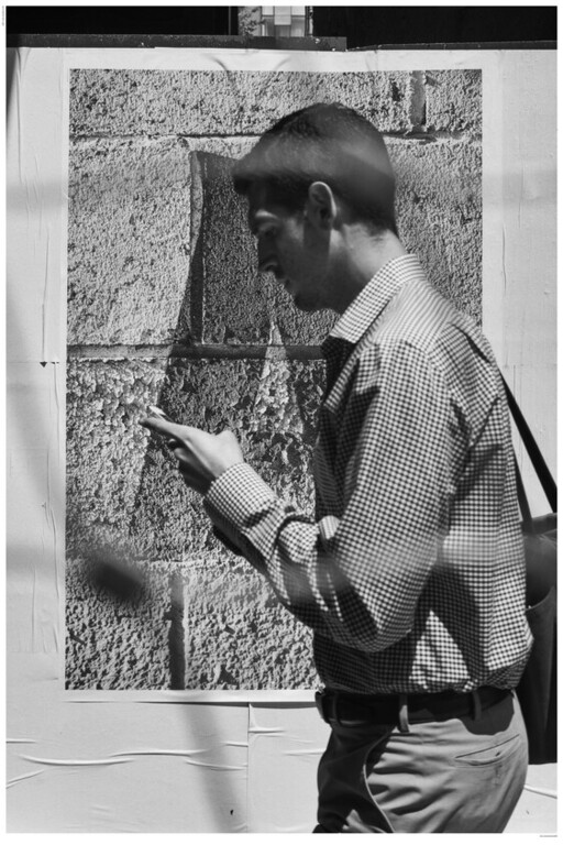 A man walks past a textured wall while looking down at his phone.