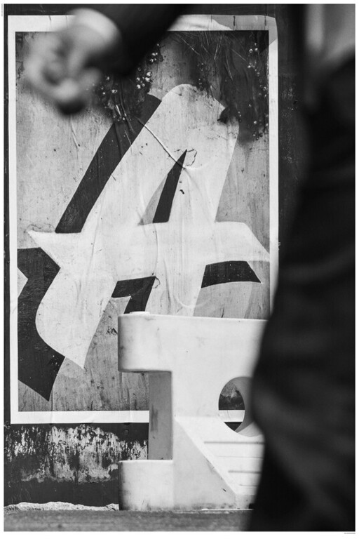Large torn letter A poster behind a concrete bench as a person walks past.