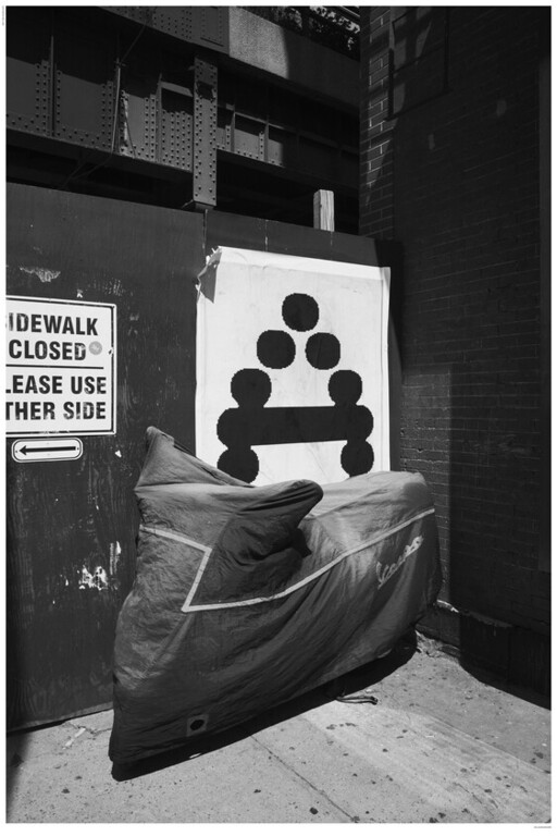 A covered motorcycle parked against a construction wall next to a sign reading "SIDEWALK CLOSED".